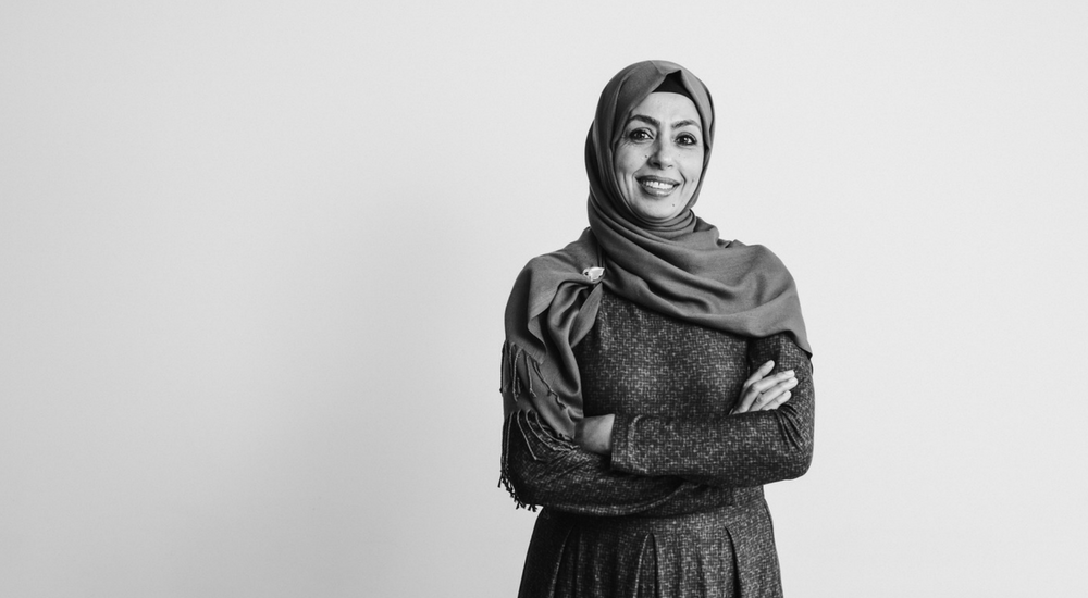 Woman in a hijab with crossed arms smiling at the camera.